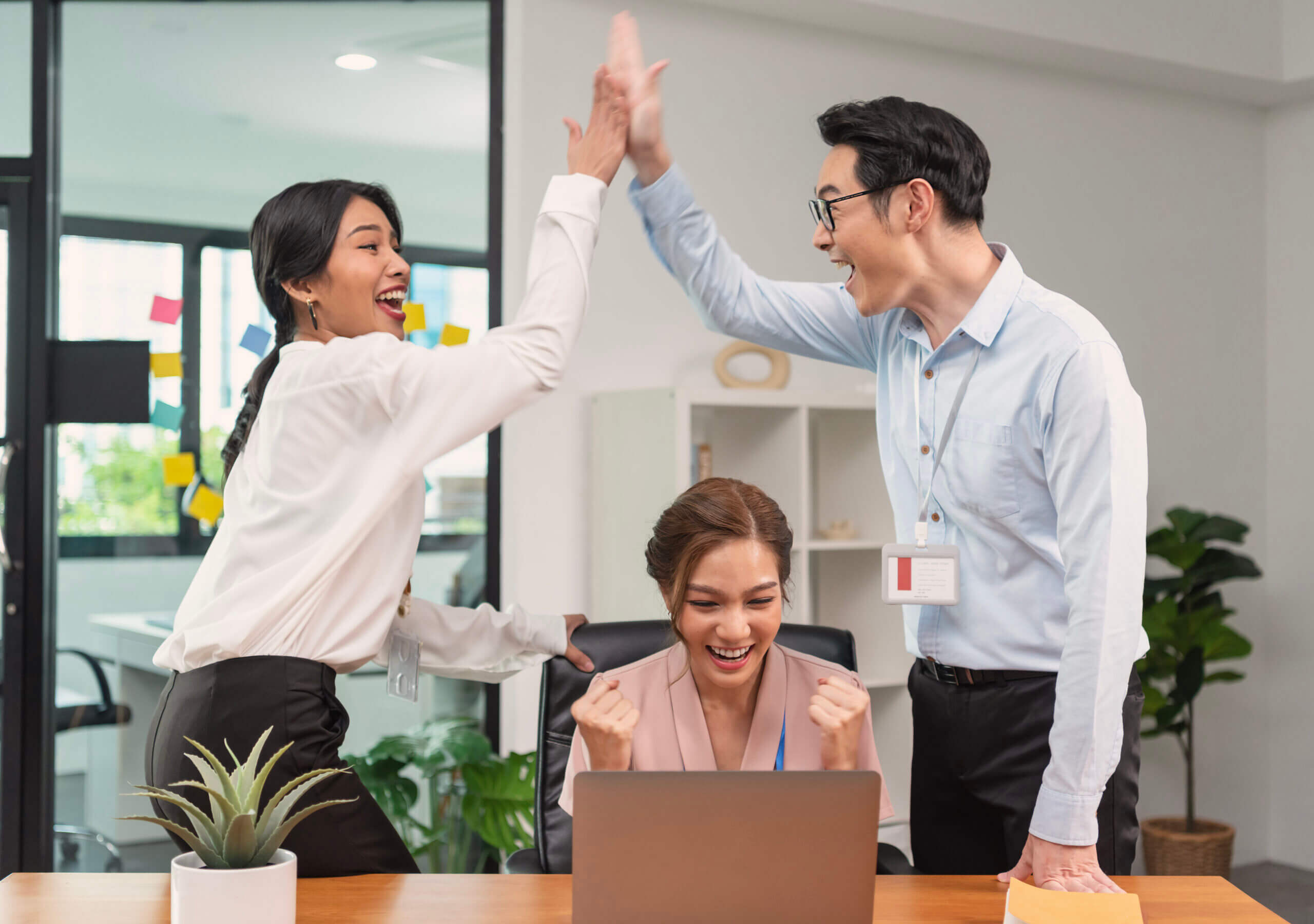 Two high-fiving professionals and one seated with a raised fist