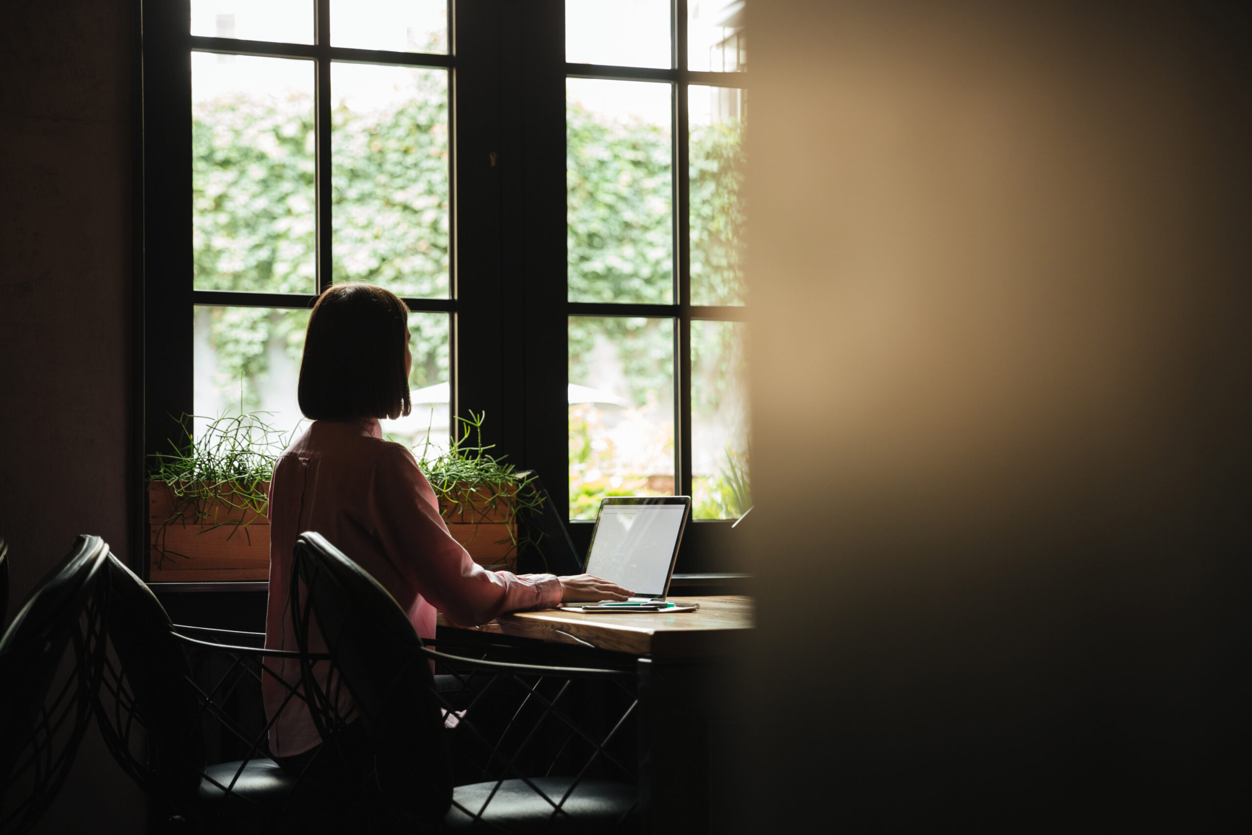 Back view of brunette woman sitting by table near window