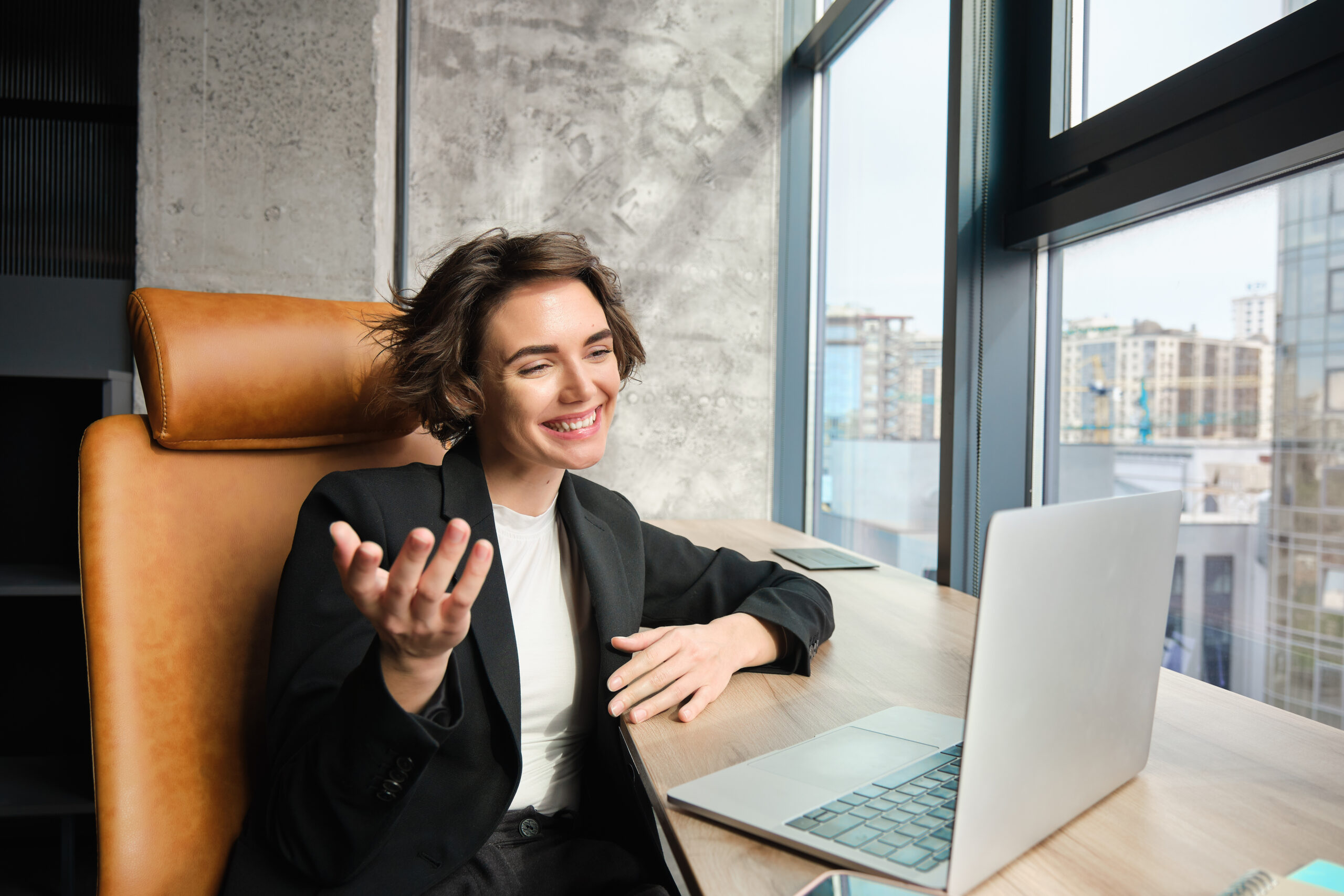 Portrait of corporate woman in office, working, giving presentation, chatting with clients or coworkers on laptop, having online meeting, wearing business suit